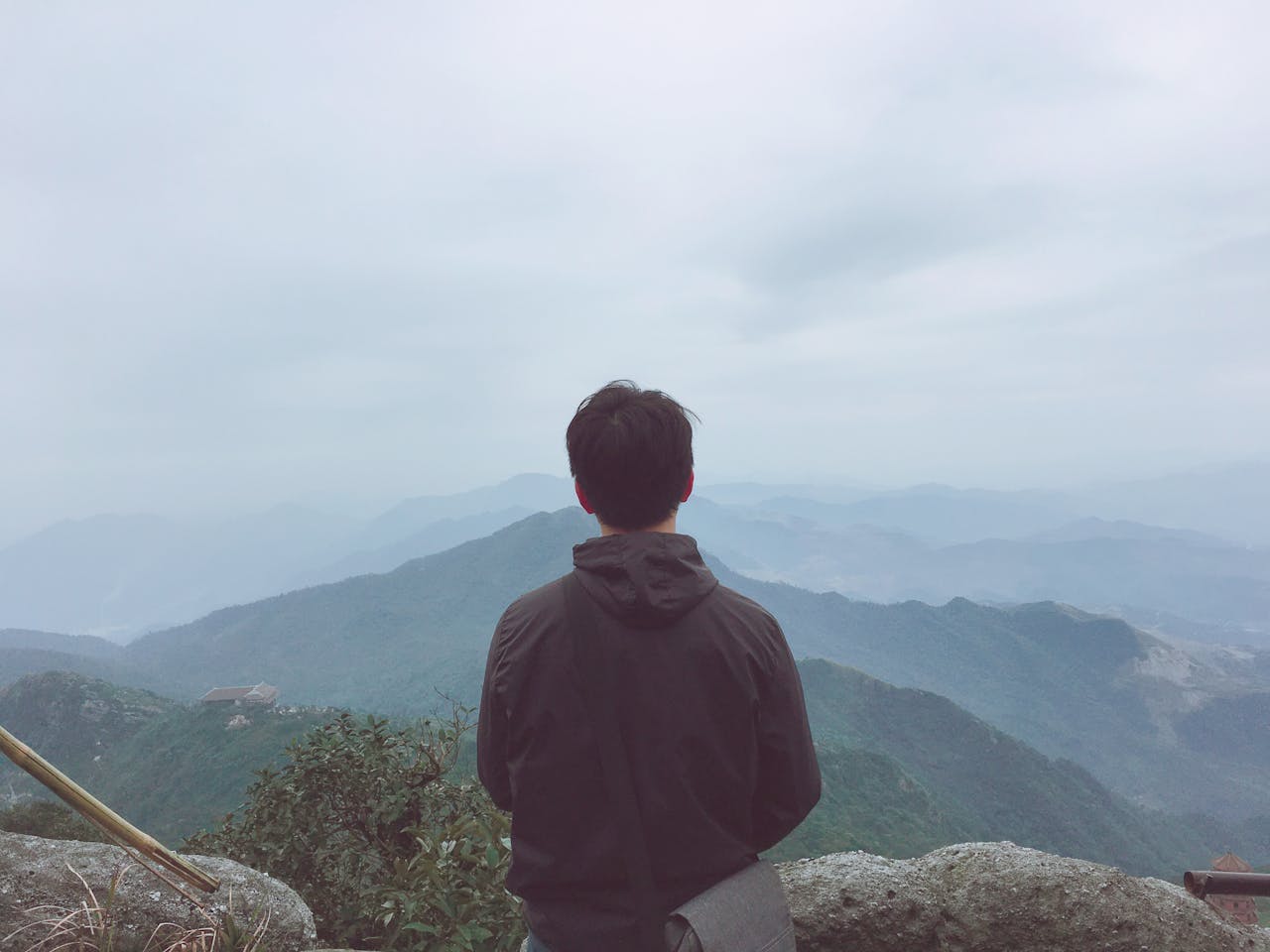 A man in a black hoodie admires a panoramic mountain view in Uông Bí, Vietnam.
