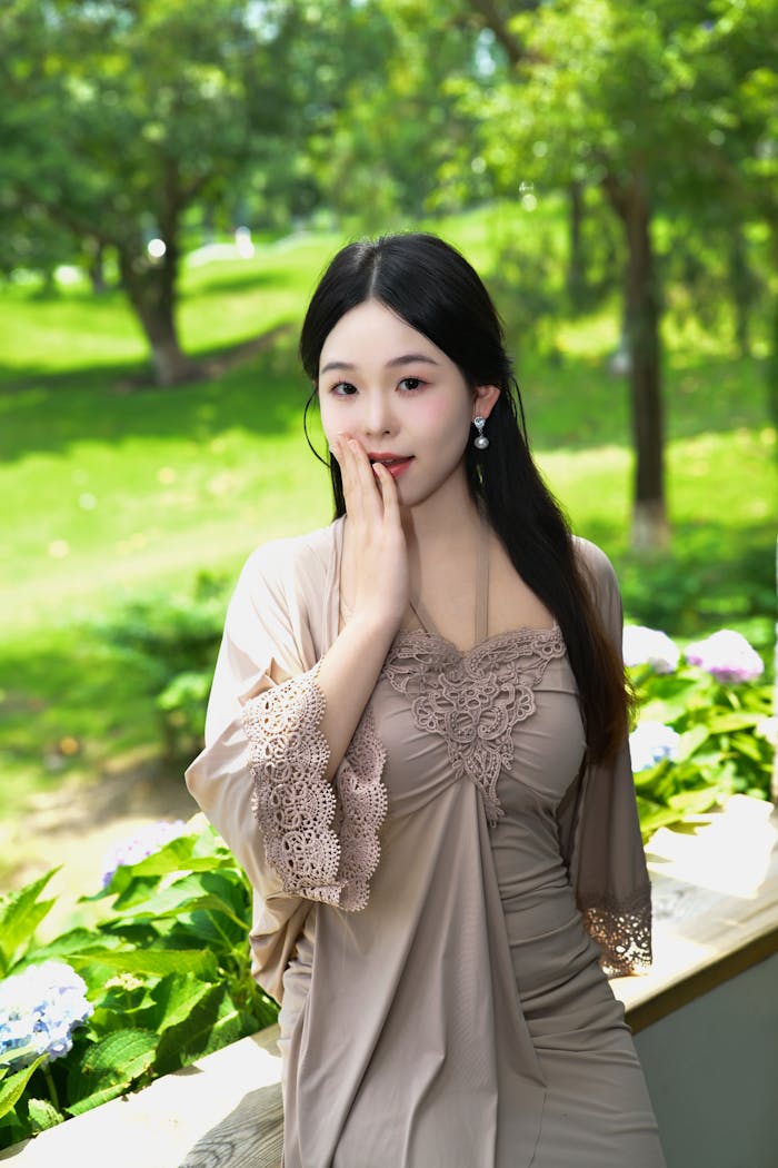 Young woman in elegant dress posing outdoors in a lush green garden.