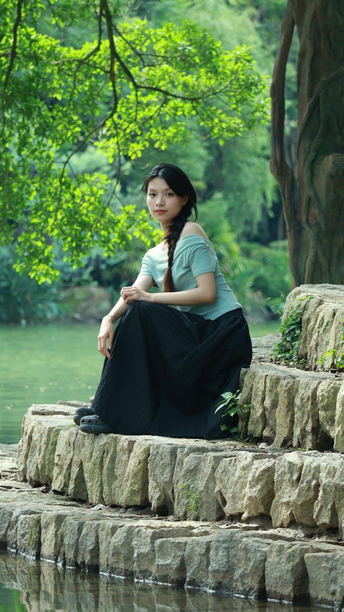 An adult woman sitting by a serene forest lake, showcasing tranquility and natural beauty.